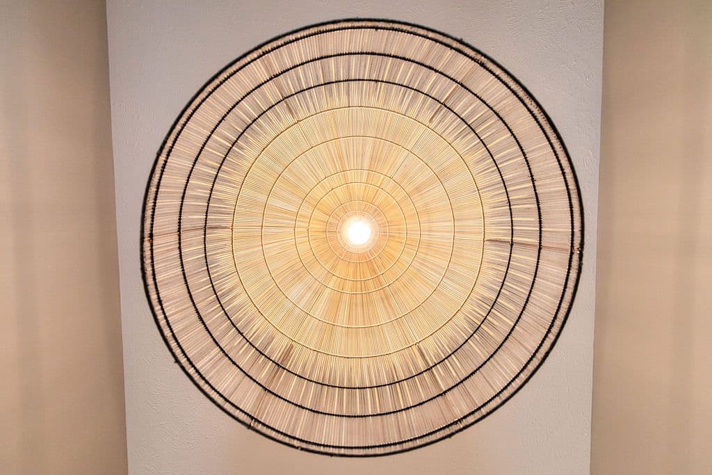 Unique light fixture with straw radial pattern on ceiling. The fixture has a circular design with rings of black twine binding the natural straw.