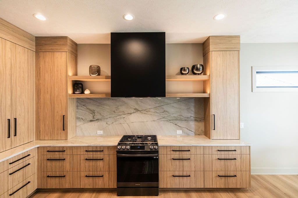Contemporary kitchen featuring light wood cabinets with black hardware, marble backsplash, and black range hood. The kitchen has open shelving, recessed lighting, and a minimalist aesthetic.