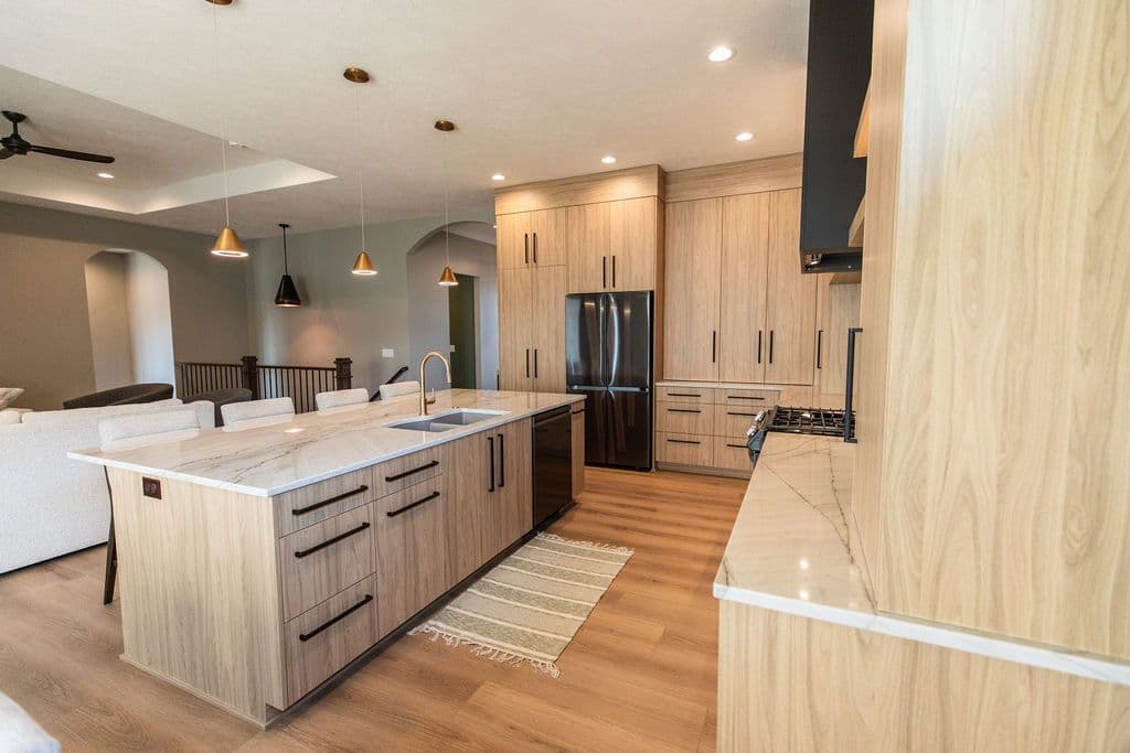 Modern kitchen with light wood cabinetry, a large marble island with a built-in sink, and black stainless steel appliances. Pendant lights hang above the island.