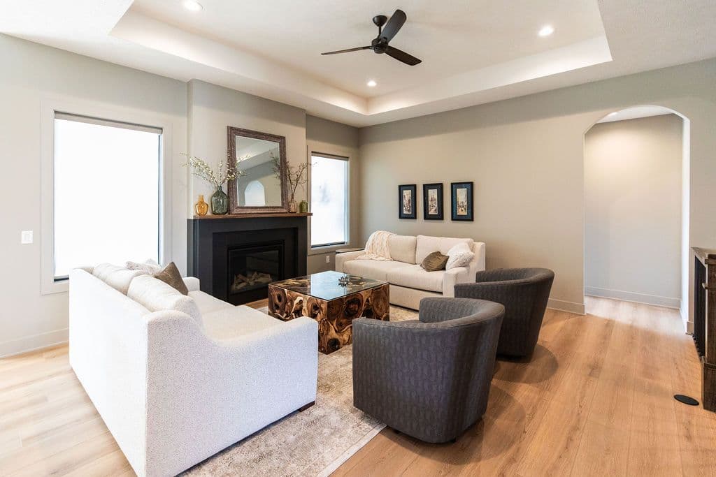 This living room features hardwood floors, a coffered ceiling with recessed lighting, and a black fireplace with a mirror above it. There are two sofas and two chairs around a wooden coffee table on a patterned rug.