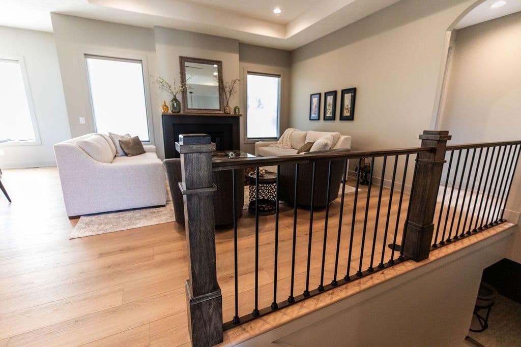 Living room featuring two sofas, two dark chairs, and wood floors, viewed from a stair landing. The space includes a fireplace with a mirror above and framed artwork on the wall, creating a cozy and inviting atmosphere.