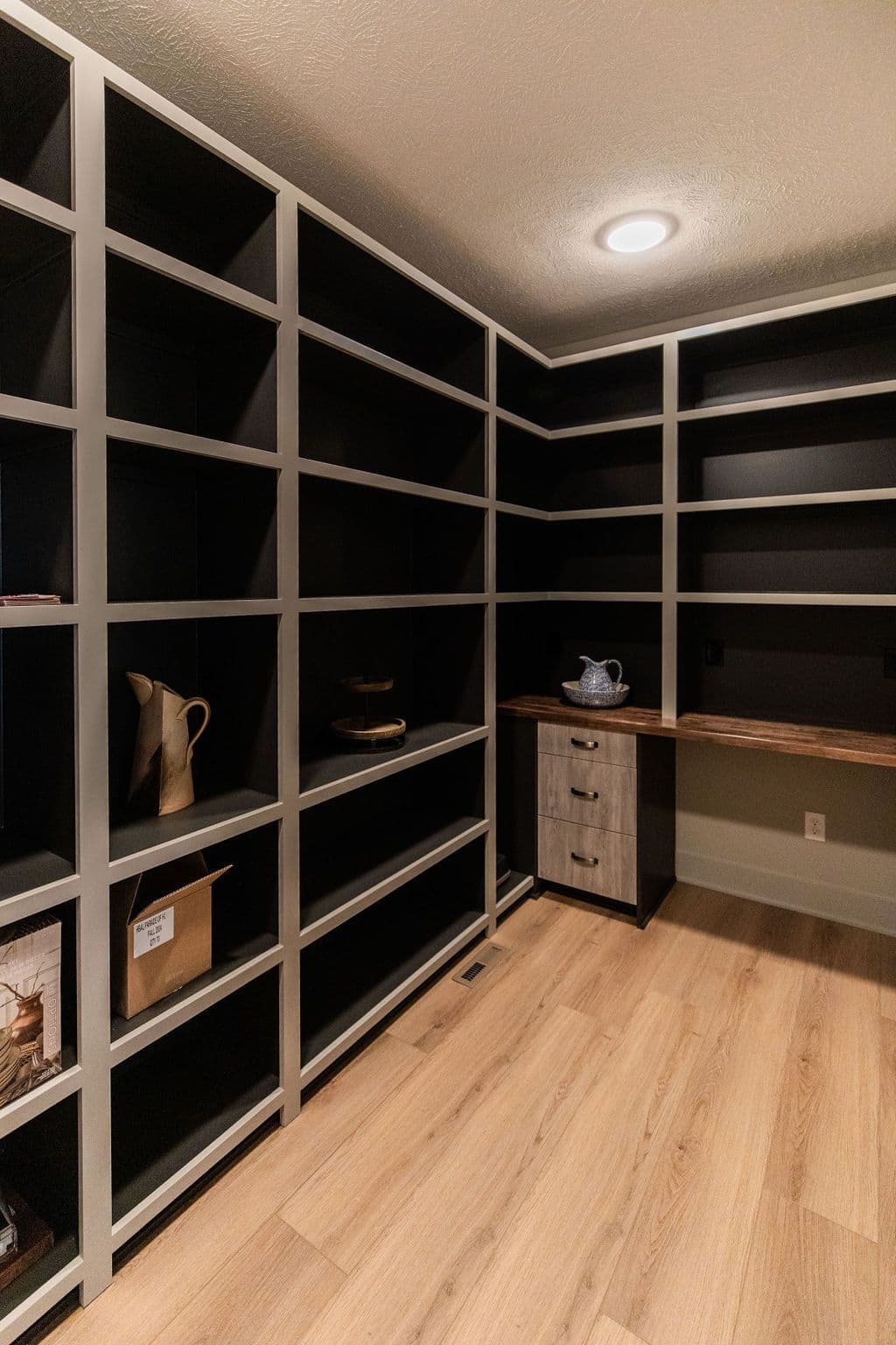Pantry features custom built-in shelving, a wooden countertop with lower cabinets, and light wood flooring. The shelves are painted black on the inside with a light gray frame.