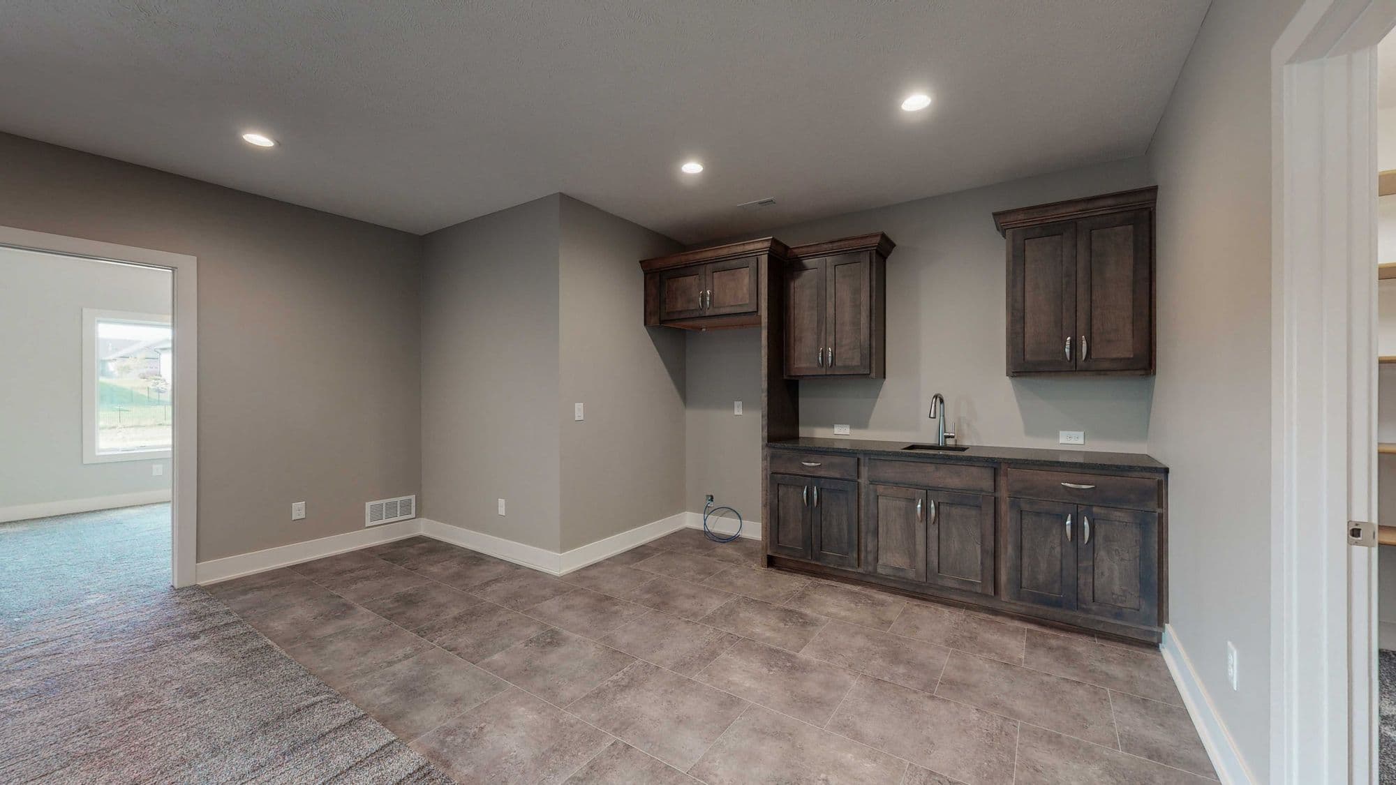 Basement area features dark wood cabinets and a wet bar. The room is finished with gray walls, tile flooring, and recessed lighting.