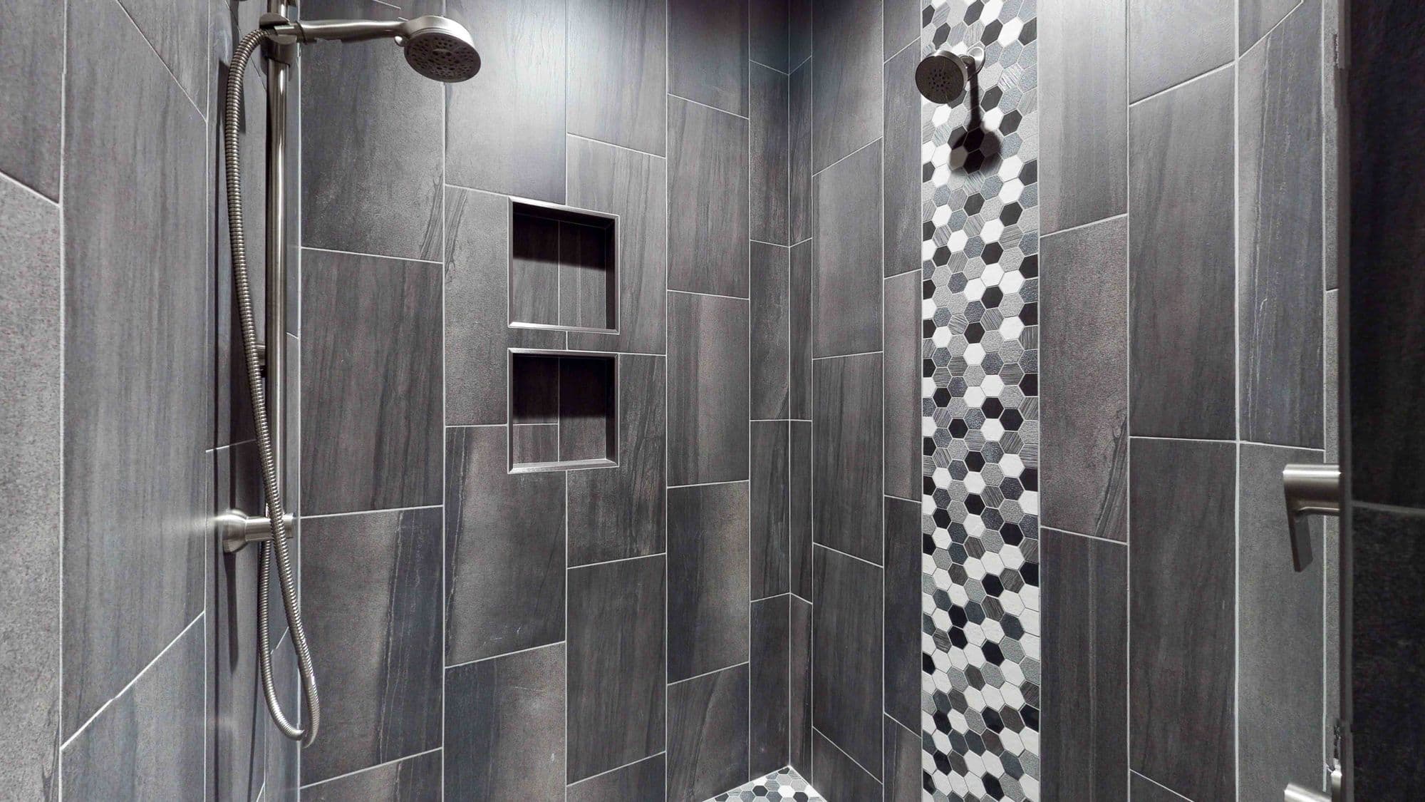 Modern shower with gray tile and a mosaic accent strip. The shower features two built-in niches and both a fixed and handheld shower head.