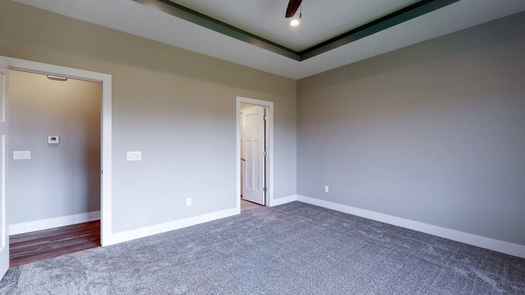 Bedroom featuring gray carpet, light gray walls, and white trim. The room has a tray ceiling with a dark green accent and two doorways with white doors.