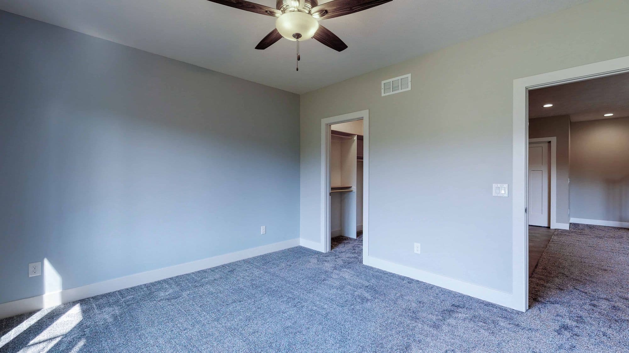A bedroom with blue carpet and a ceiling fan is pictured. A closet and doorway leading to another room are also visible.