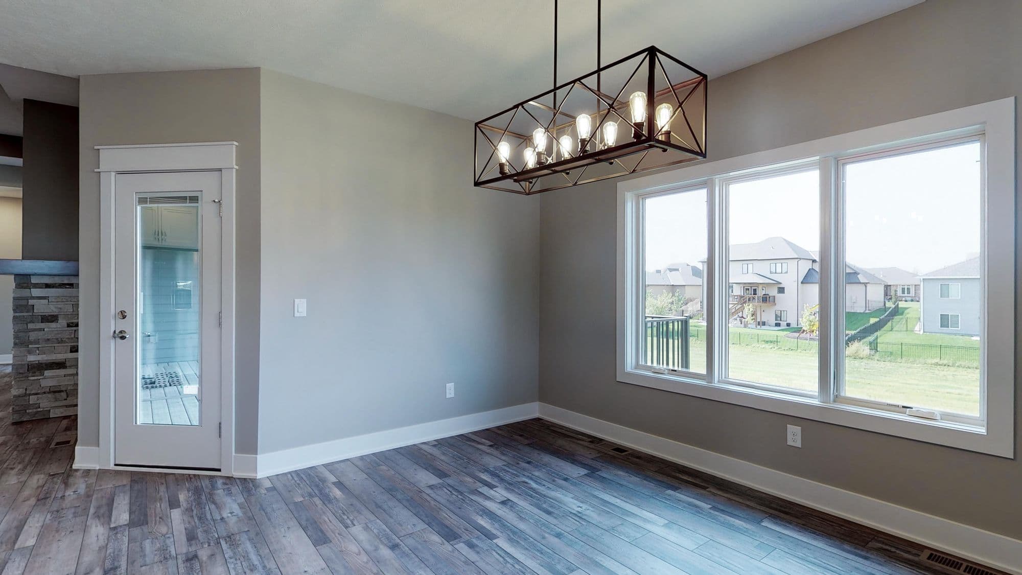 Dining room area features a modern chandelier, large windows overlooking a backyard, and hardwood flooring. The room is painted in neutral tones with white trim.