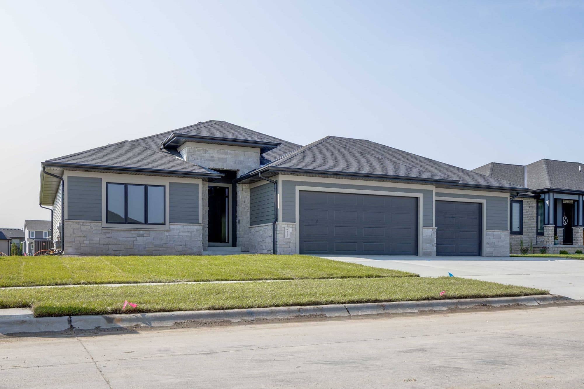 Modern single-family home featuring a combination of gray horizontal siding and stone veneer. The house has a two-car attached garage, a dark gray asphalt shingle roof, and well-maintained green lawn.