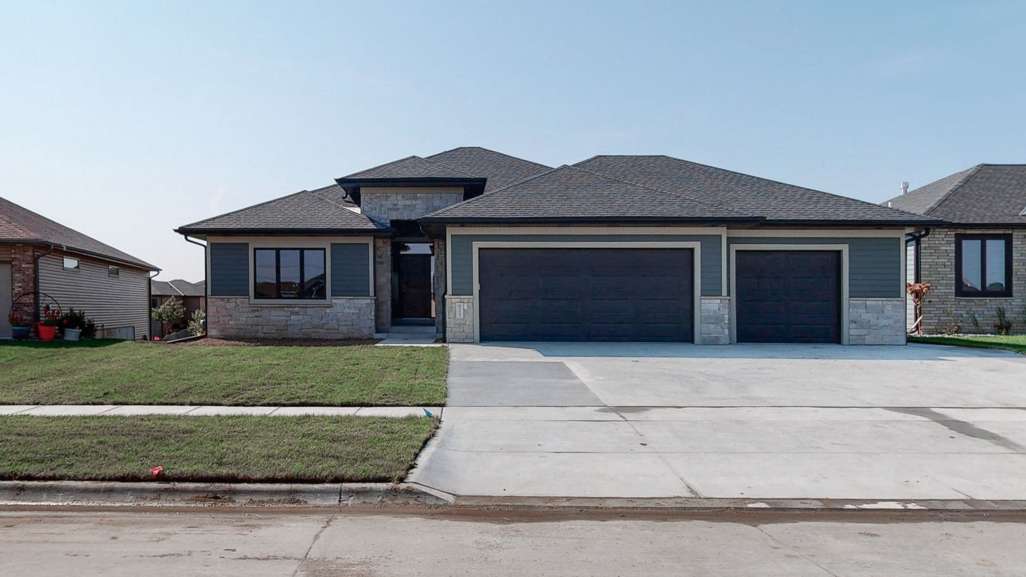 Modern home exterior featuring a two-car attached garage, stone veneer accents, and horizontal siding. The roof is asphalt shingle with a mix of well-manicured lawn and concrete driveway.