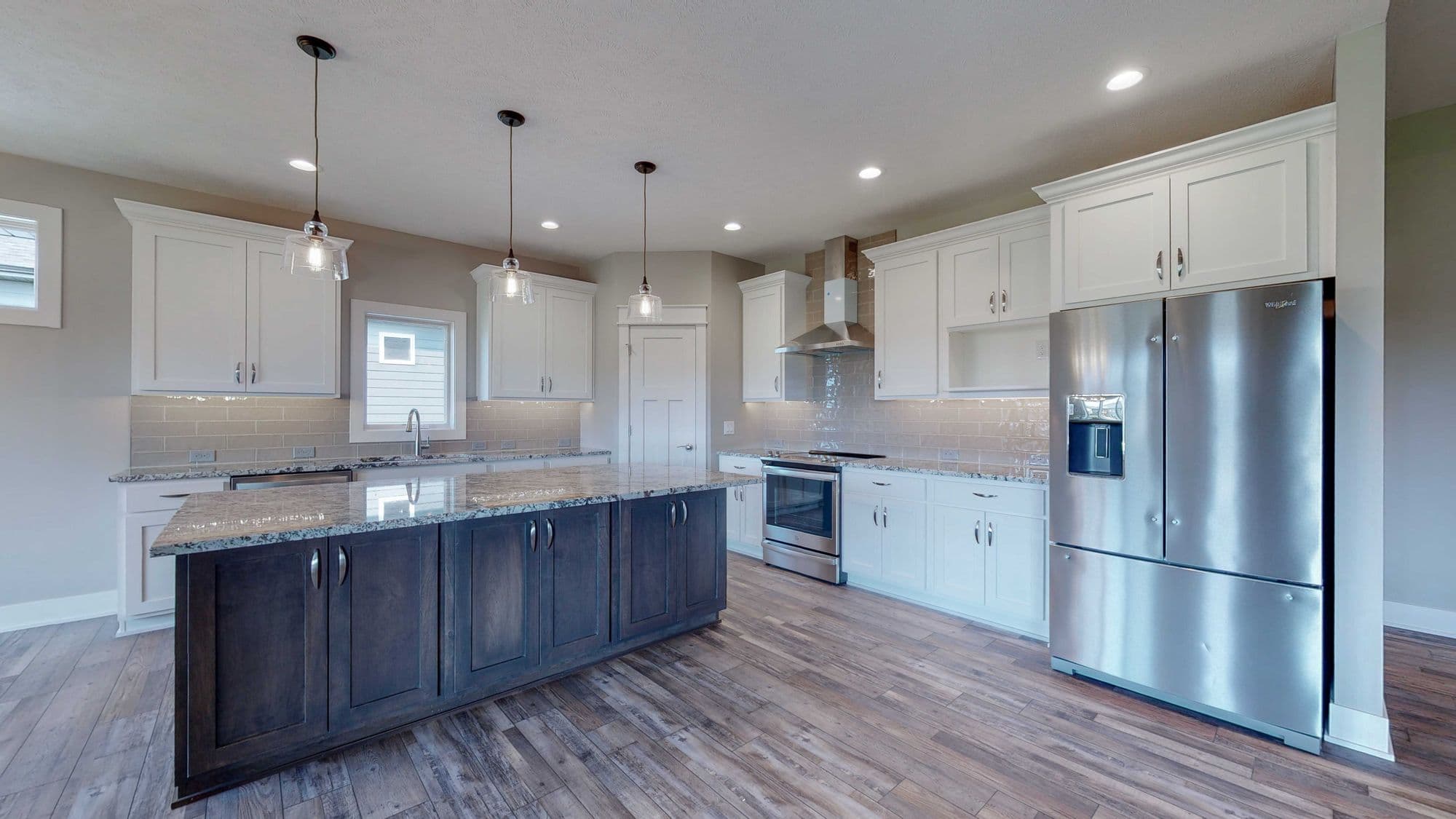 Modern kitchen with white cabinetry and a dark stained island illuminated by pendant lights. Stainless steel appliances and hardwood flooring complete the space.