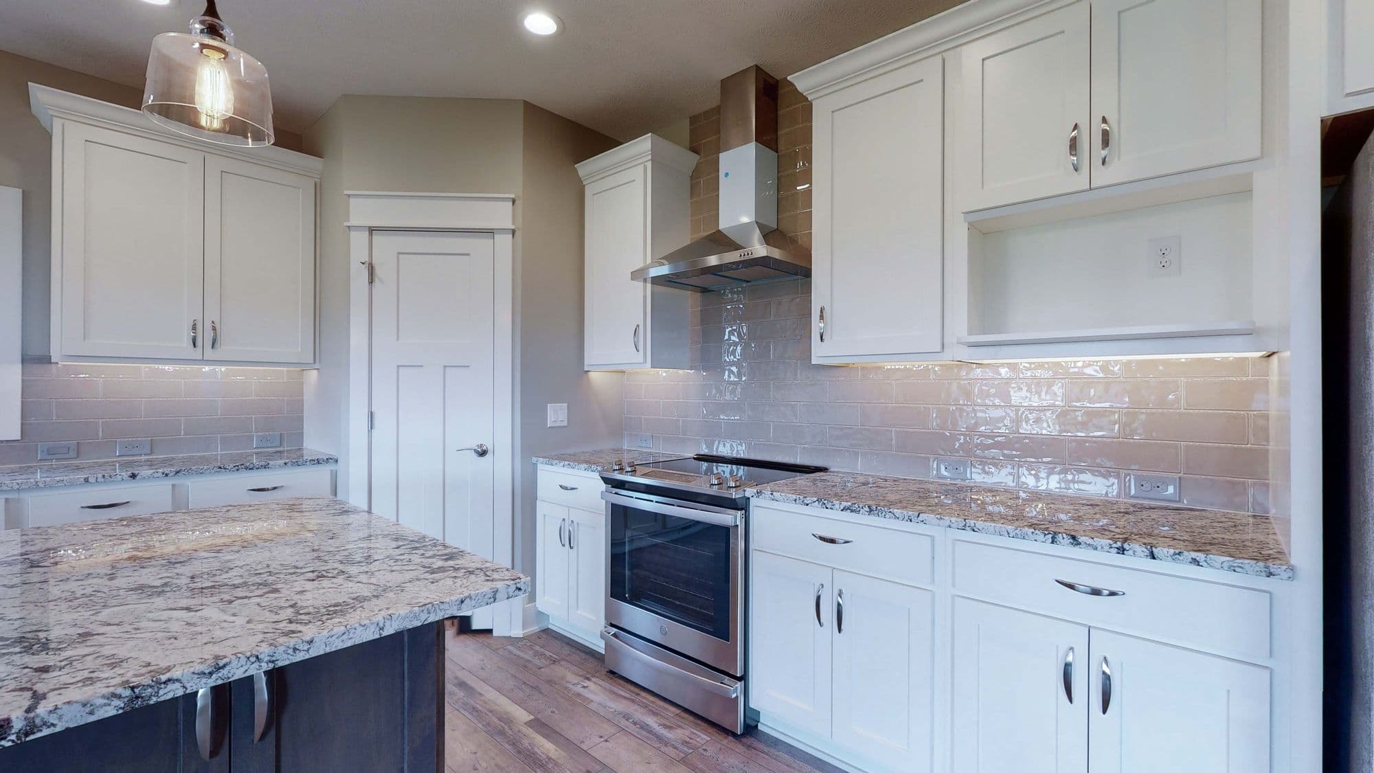 Bright kitchen features white cabinetry, granite countertops, and stainless steel appliances. An island with a dark base offers extra counter space.