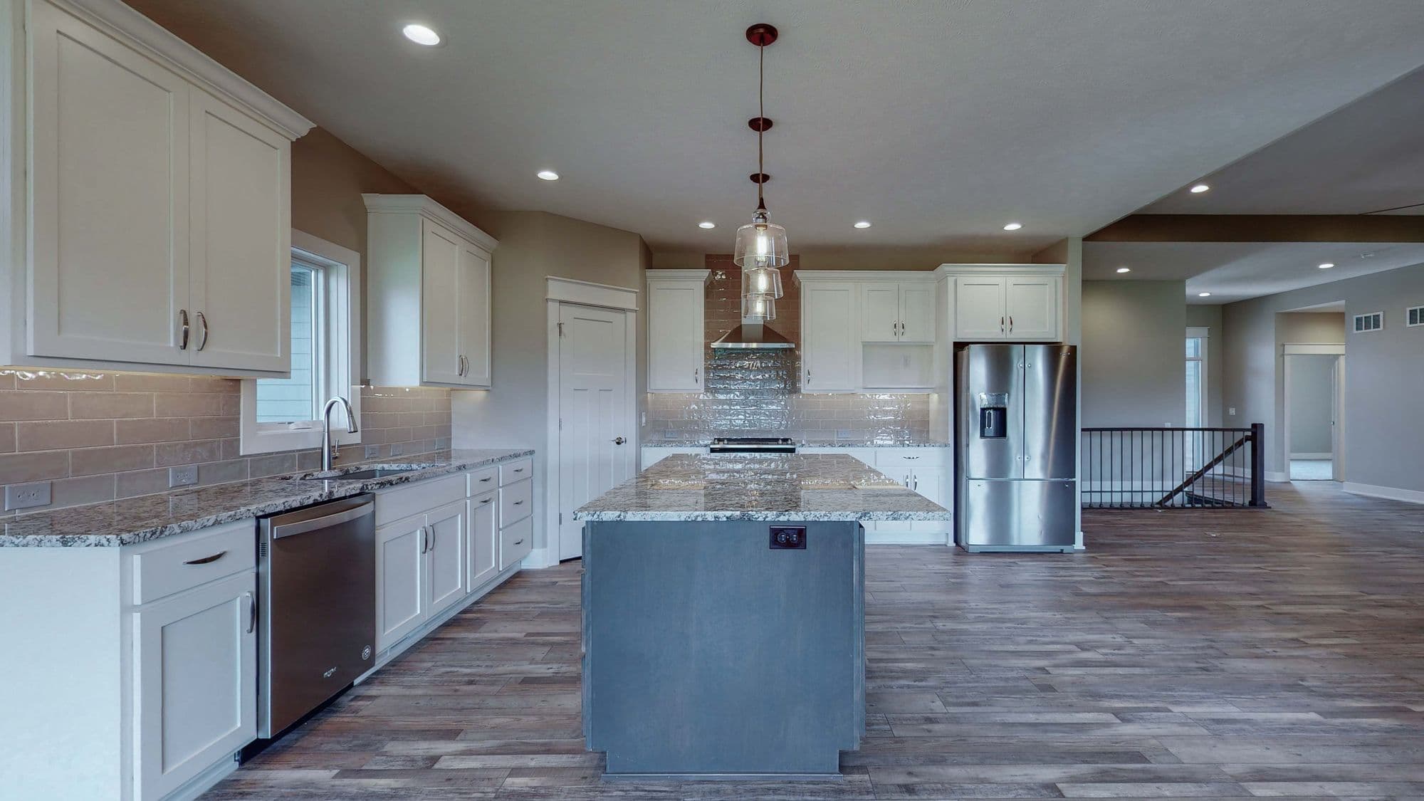 A modern kitchen features white cabinetry, granite countertops, and stainless steel appliances. A gray island sits centrally under pendant lighting.