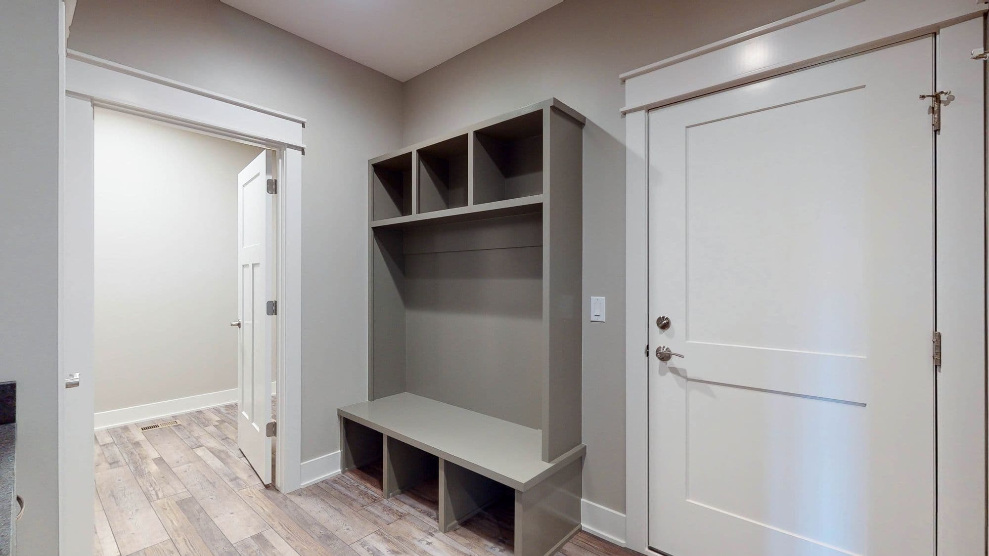 Mudroom with custom gray built-in bench and storage. The floor is wood-look tile and the doors are white.