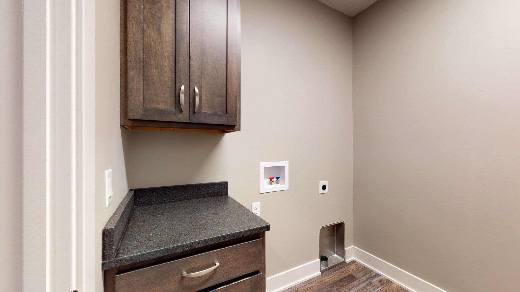 Laundry room features dark wood cabinets, granite countertops, and wood-look flooring. The room includes a white utility sink box and hookups for a washing machine.