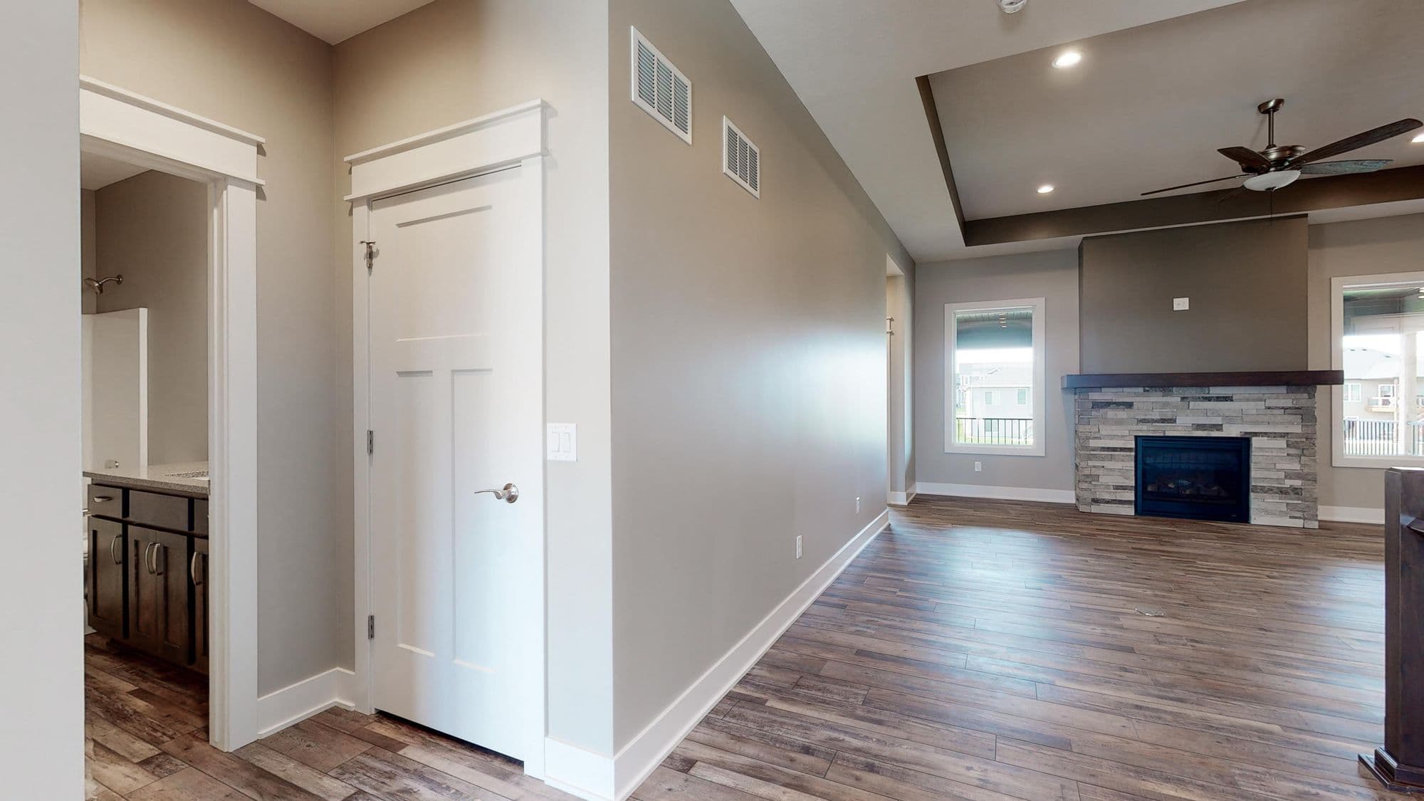 Interior view of a home featuring hardwood floors and neutral walls. The space includes a doorway leading to a bathroom, a white door, and an open living room area with a fireplace.