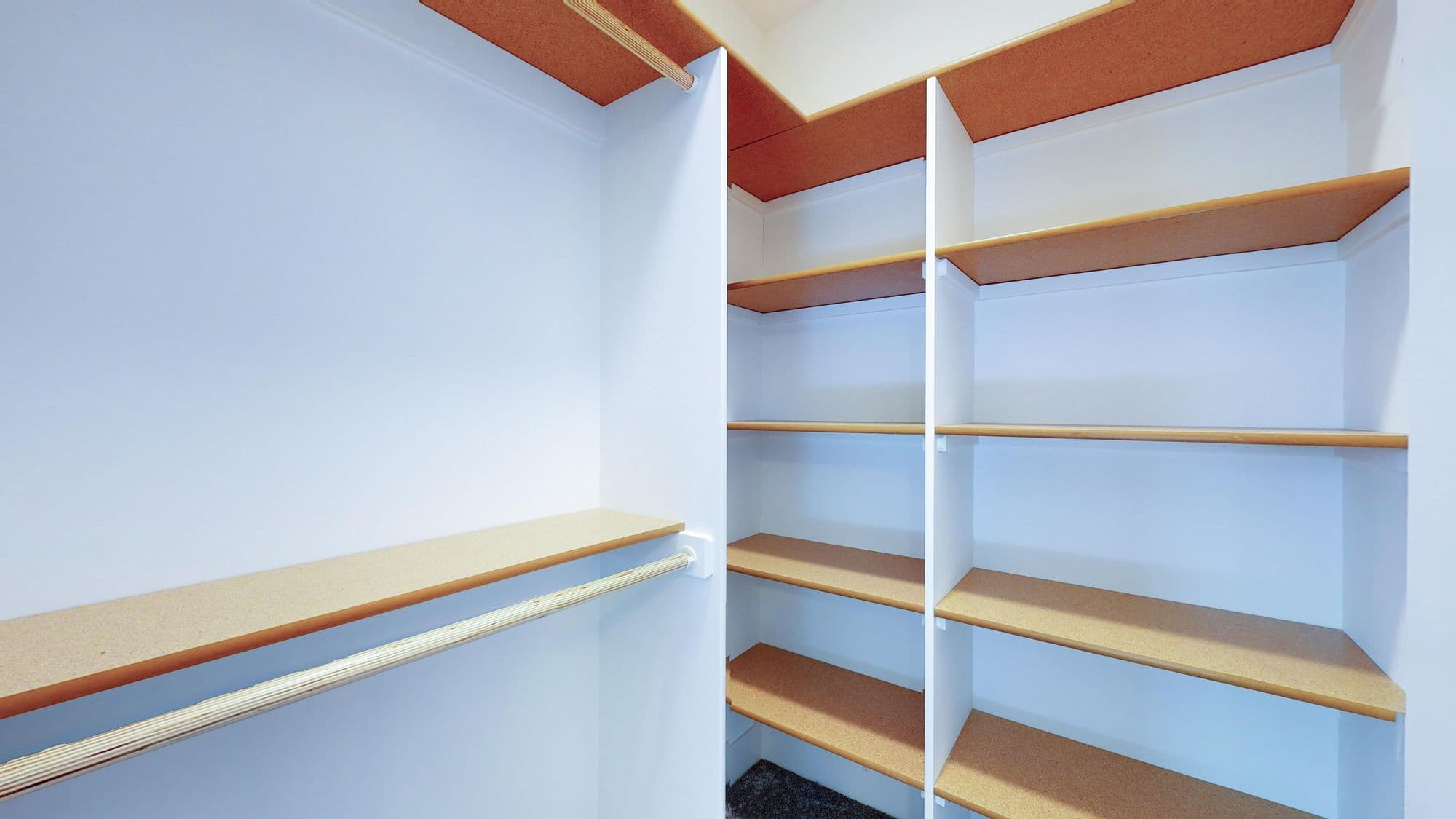 Walk-in closet with custom shelving and hanging rod. Shelves are white and tan and the walls are painted white.