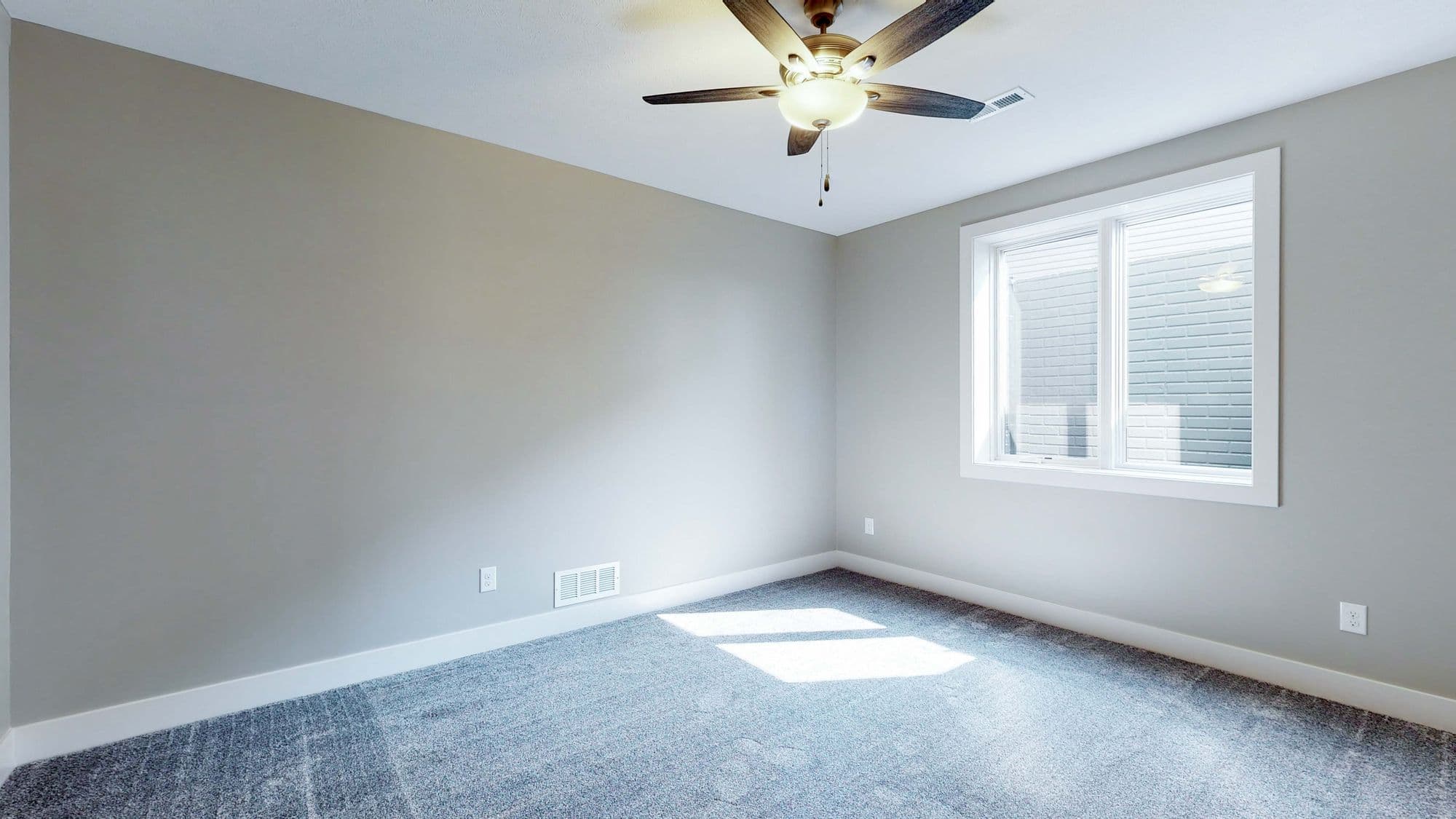 Neutral bedroom features light gray walls, a ceiling fan, and a white-framed window. The room is carpeted with a blue-gray carpet and has white baseboards.
