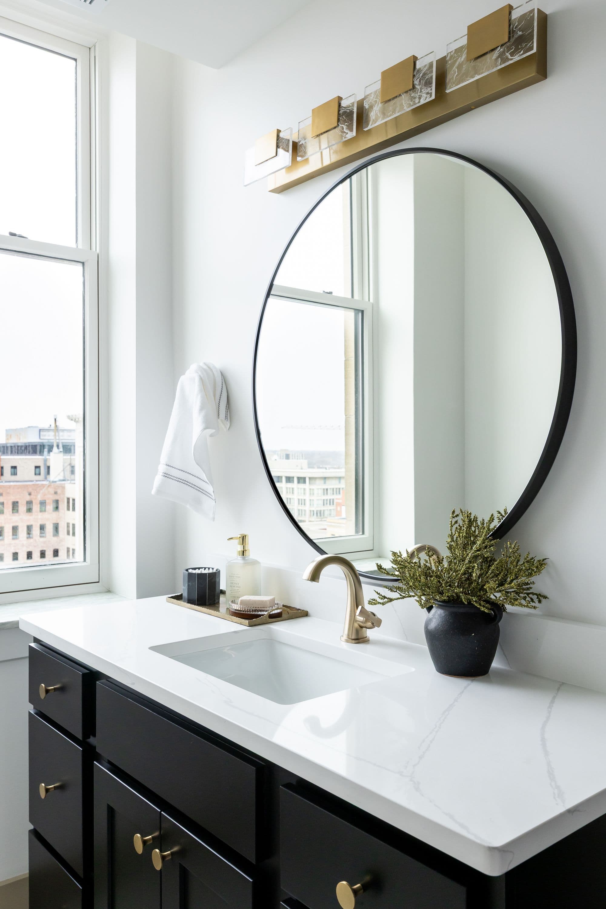 Bathroom features a black vanity with gold hardware, white quartz countertop, and oval mirror. A gold faucet and decorative pot add to the space's elegance.